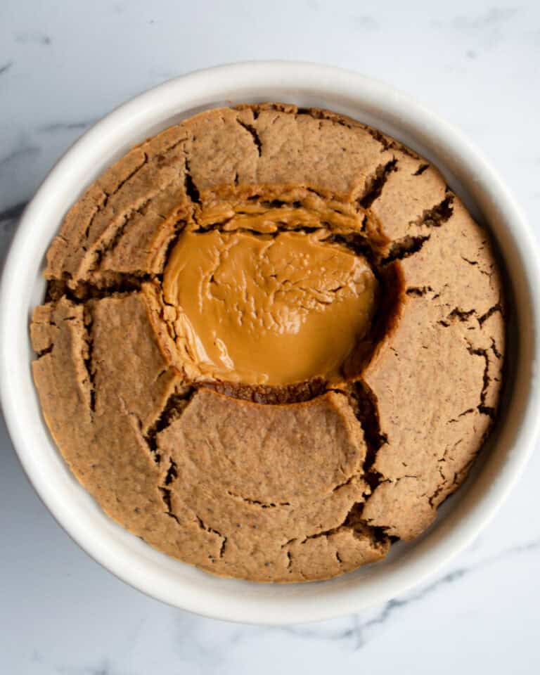 Soft-baked peanut butter skillet cookie with melted peanut butter center in a white ramekin on marble surface.