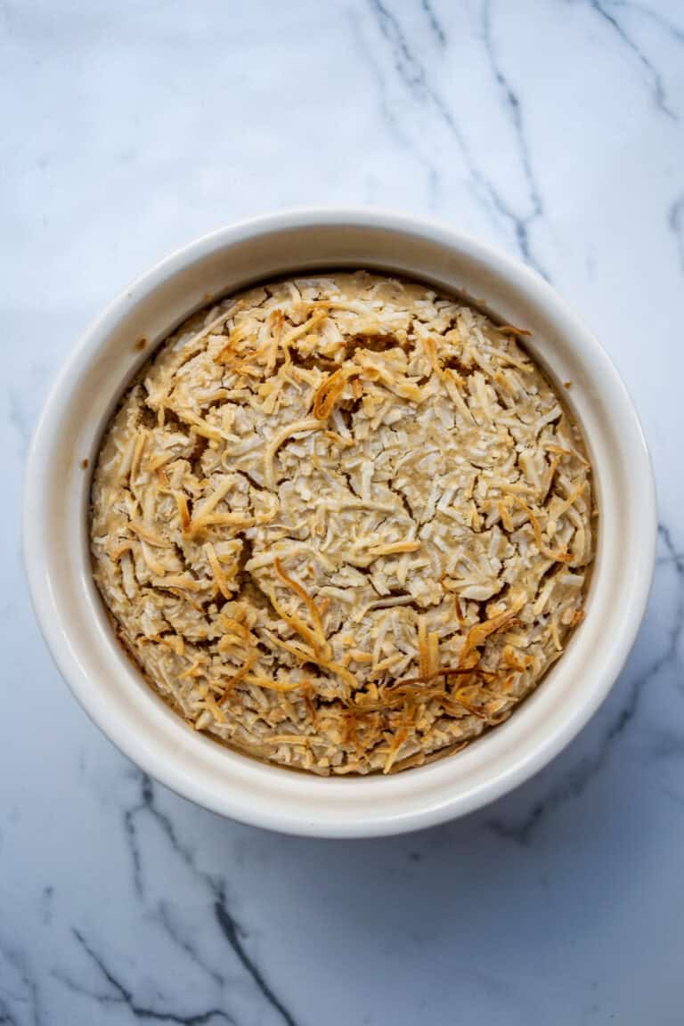 Creamy baked chicken pot pie topped with shredded cheese in a white ramekin on a marble surface.