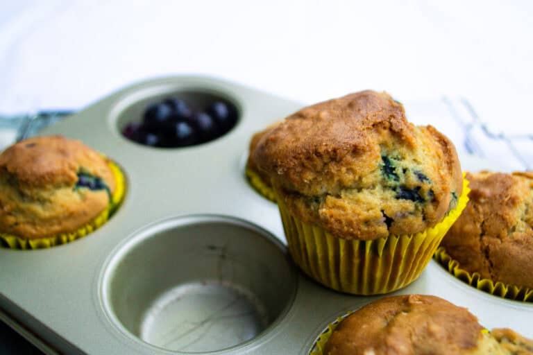 Fluffy blueberry muffins in a muffin tin, fresh out of the oven, with a few blueberries visible inside, perfect for breakfast or snack.