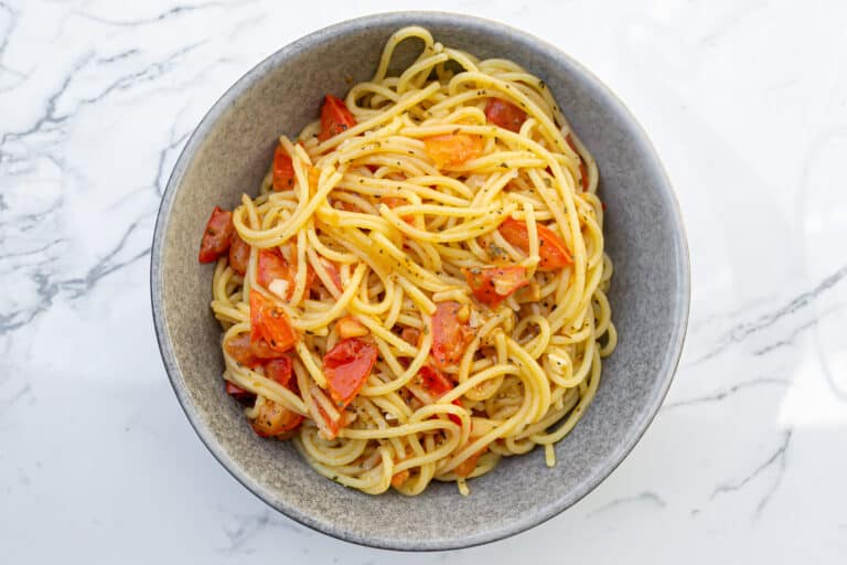 Savory spaghetti pasta with cherry tomatoes and herbs served in a gray bowl on marble surface.