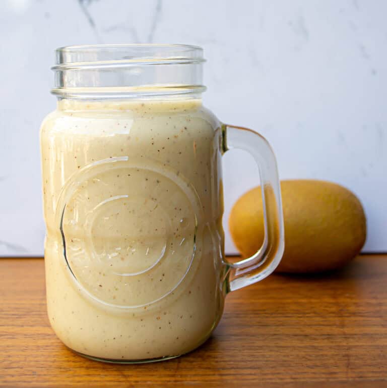 Creamy homemade mango smoothie in a glass jar with fresh mango in the background, perfect for a healthy breakfast or snack, high in vitamins and delicious fruit flavors.