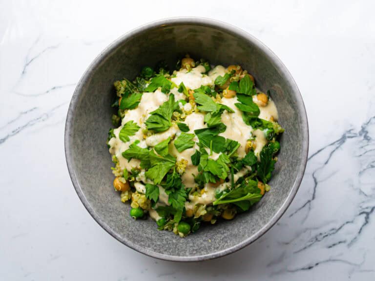 Creamy vegetable salad with peas, chickpeas, and fresh parsley in a gray bowl on a white marble surface.