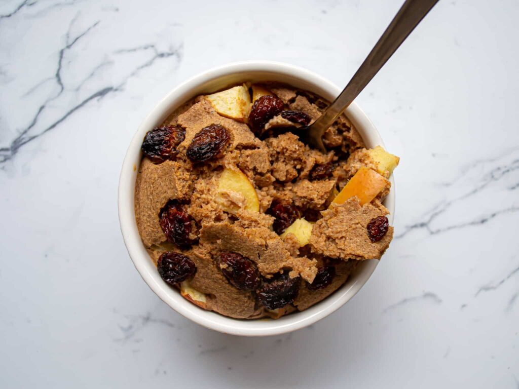 Apple baked oatmeal in a ramekin with a spoon and topped with raisins.