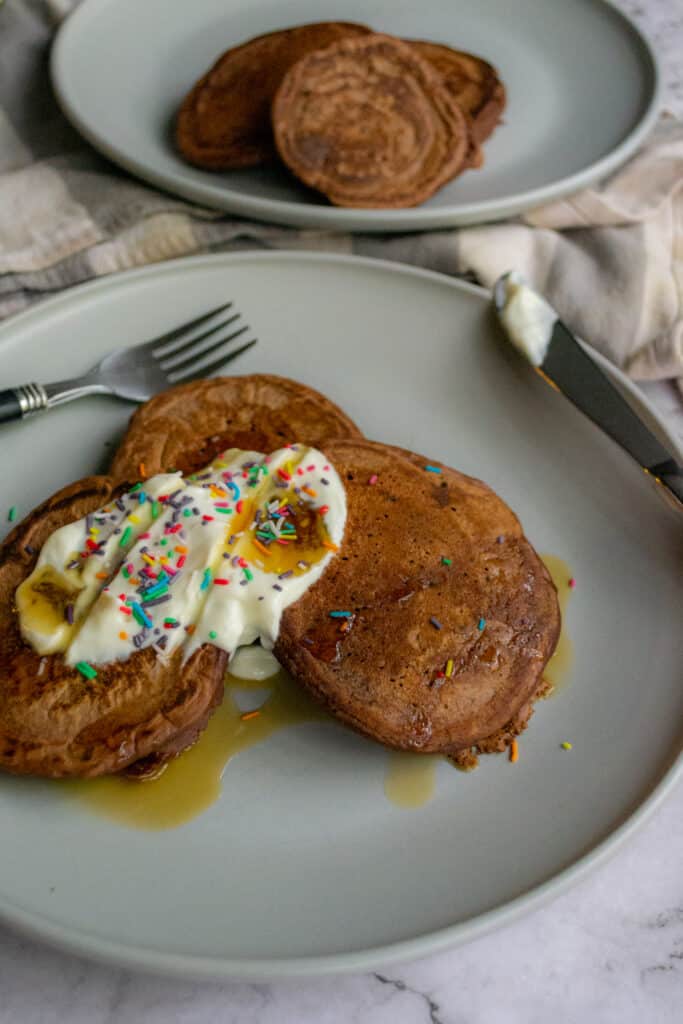 Healthy chocolate pancakes up close with a yogurt topping, rainbow sprinkles, and syrup.