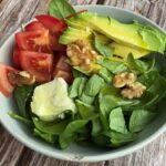 salad bowl containing spinach, avocado, tomato, goat cheese and walnuts