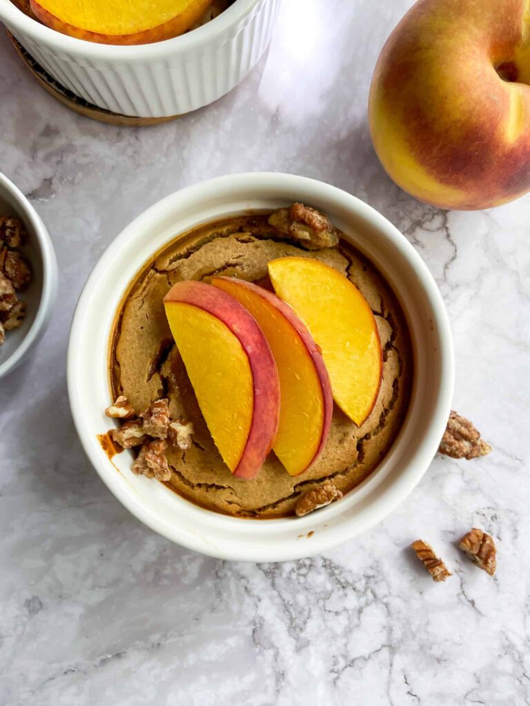 peach baked oatmeal in a ramekin with a peach and nuts next to it