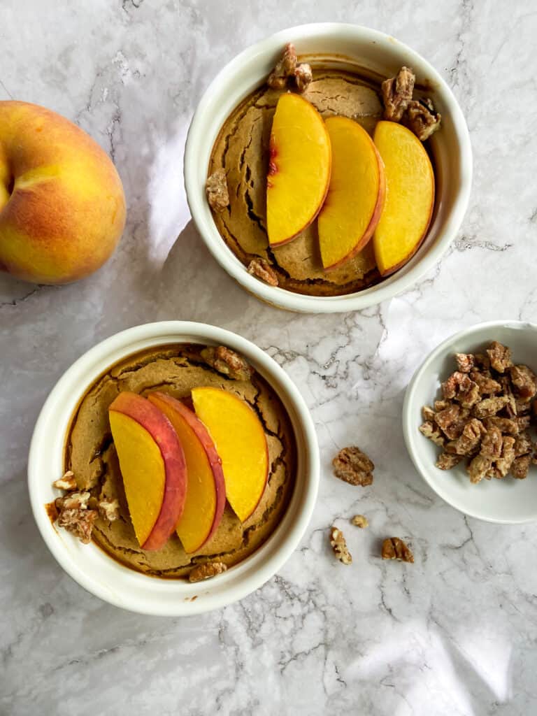 peach baked oatmeal on a marble table with a peach and a bowl of nuts
