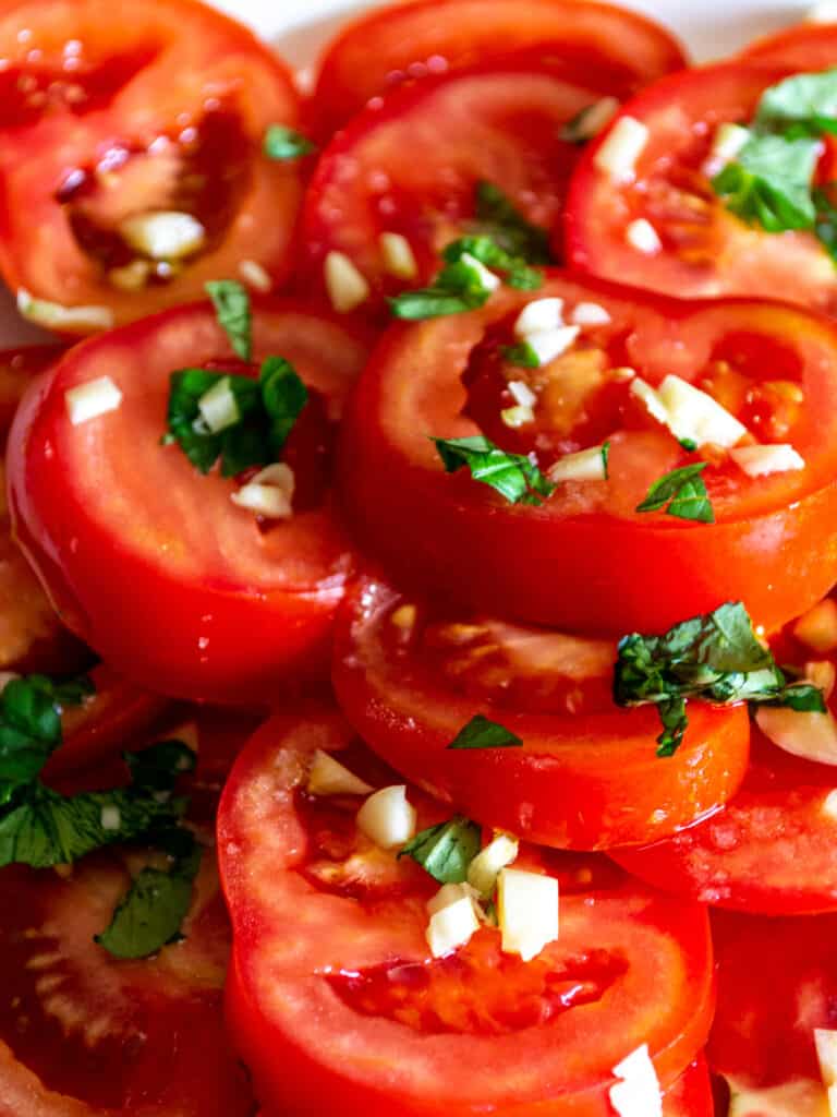 Close up of tomato salad, showing chopped basil and garlic on top of tomato slices.