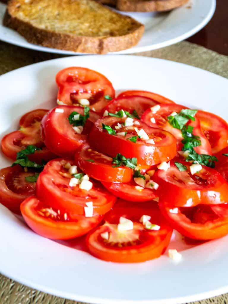 Side view of tomato salad on a plate with toasted bread in the background.