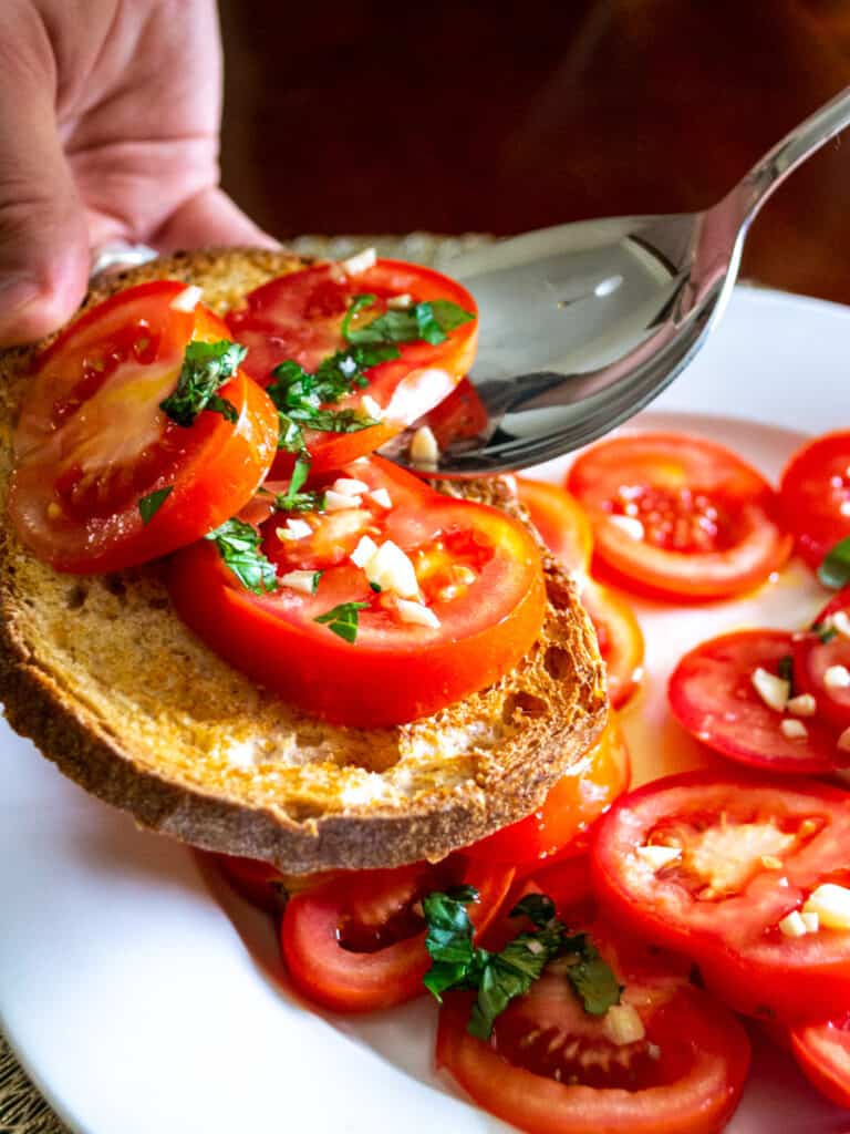 Close up of someone serving tomato salad onto a slice of toasted bread.