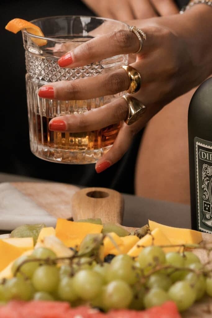 Close up of hand holding a glass of rum, with a cheese plate in the foreground.