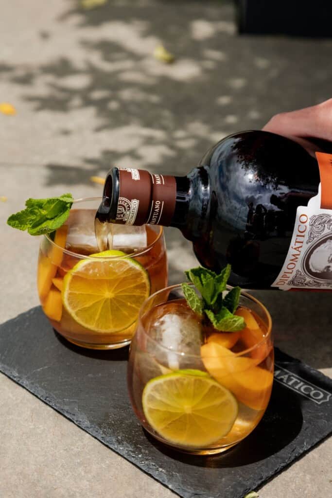 Two glasses with citrus slices in them, and rum is being poured into the glasses.