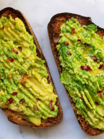 Two pieces of toasted sourdough bread, topped with smashed avocado and red pepper flakes.