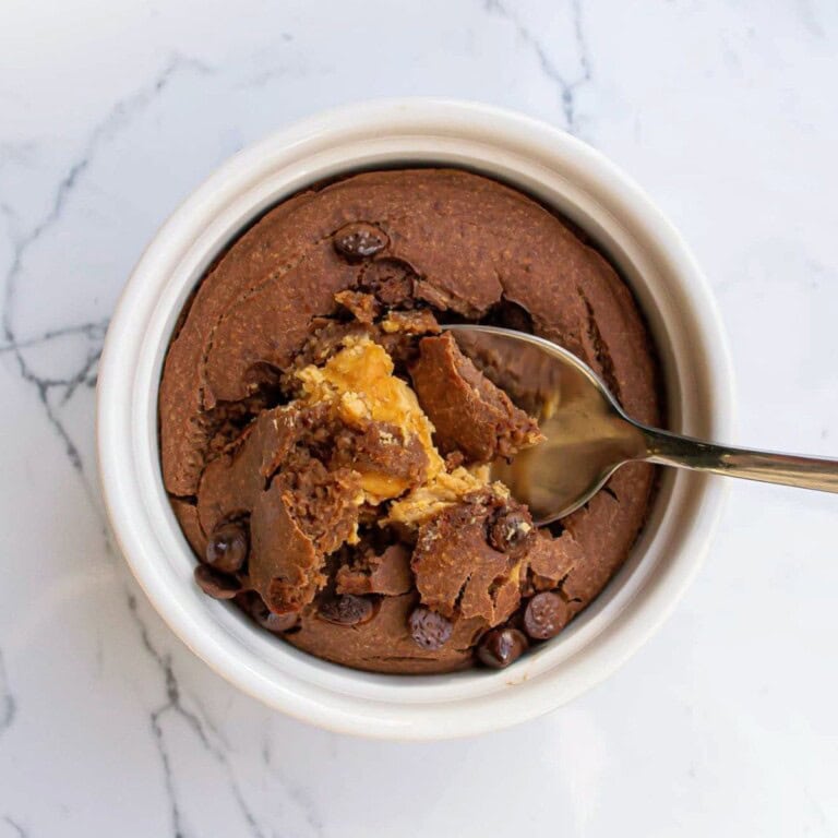 Rich, gooey chocolate chip cookie dough in a white ramekin with a spoonful taken out, showcasing the melt-in-your-mouth texture and soft center, perfect for homemade desserts and baking recipes.