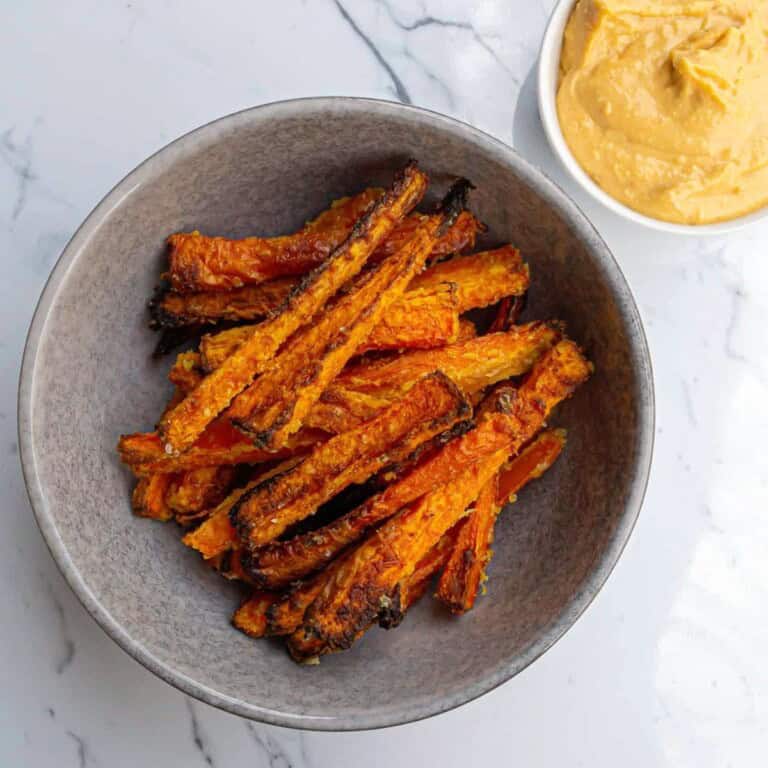 Crispy oven-baked sweet potato fries served in a grey bowl with a side of creamy dip on a white marble surface, highlighting healthy and delicious snack options.