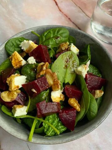 Bowl of beetroot and spinach salad with goat cheese and walnuts on top.