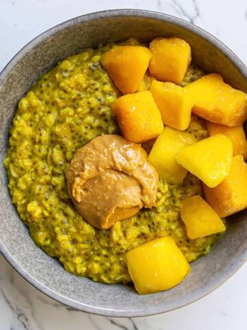 Overhead shot of yellow turmeric oatmeal in a grey bowl with mango and peanut butter on top.