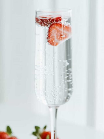 Vodka soda in a champagne glass, with a strawberry floating in it.