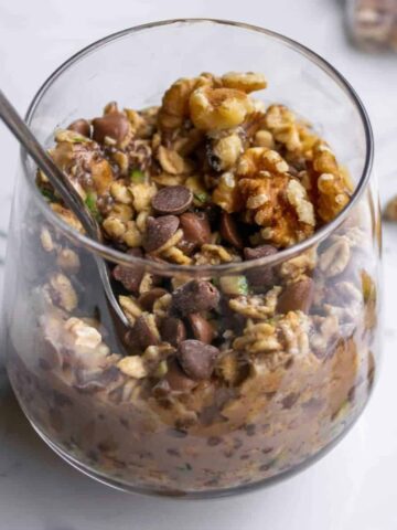 Zucchini bread overnight oats in a glass, with walnuts and chocolate chips on top.