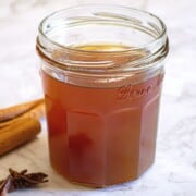Fig simple syrup in a glass jar with spices including cinnamon and star anise in the background.