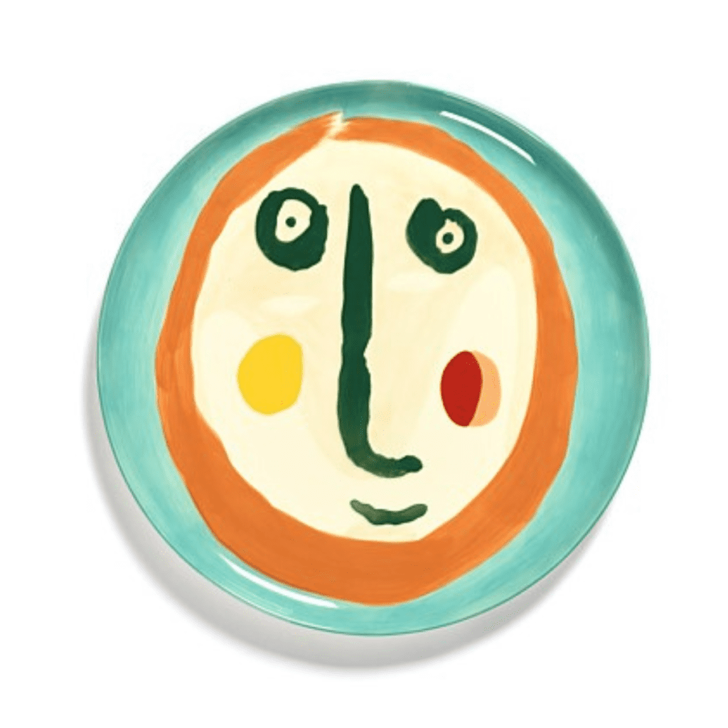 An Ottolenghi plate featuring a hand-painted face with a big green nose, coloured cheeks and an orange outline against a blue background.