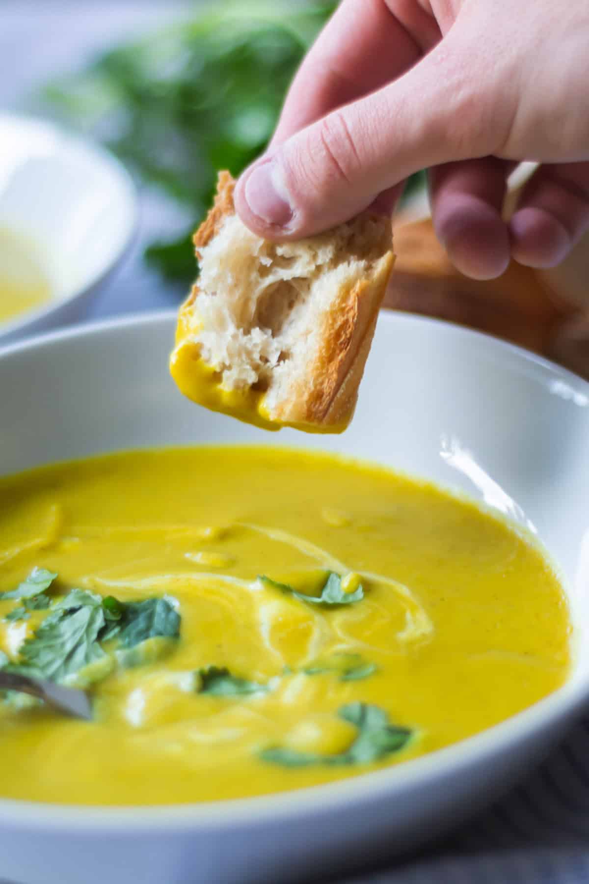 A close-up of a hand dipping a piece of bread into butternut squash soup.