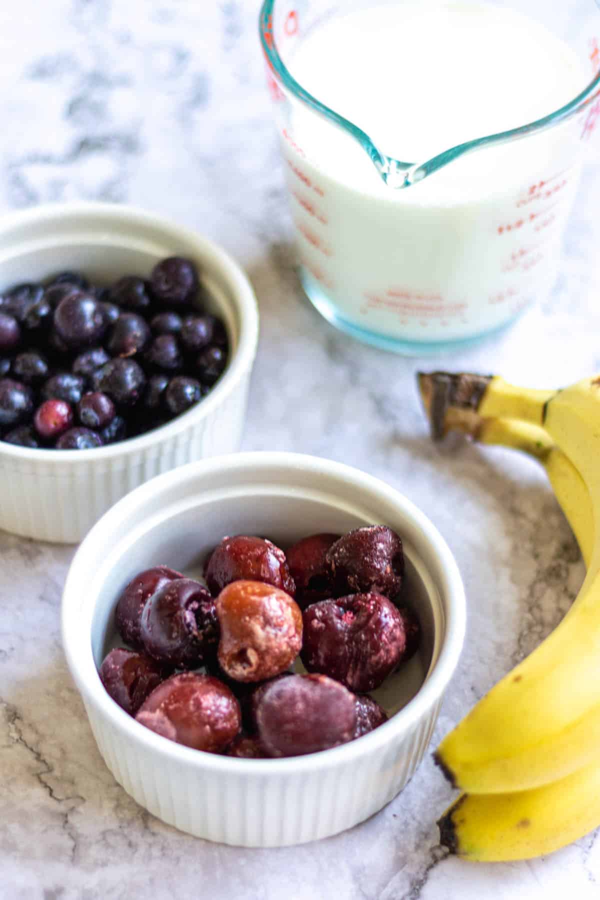 Smoothie ingredients including cherries, blueberries, bananas, and milk.