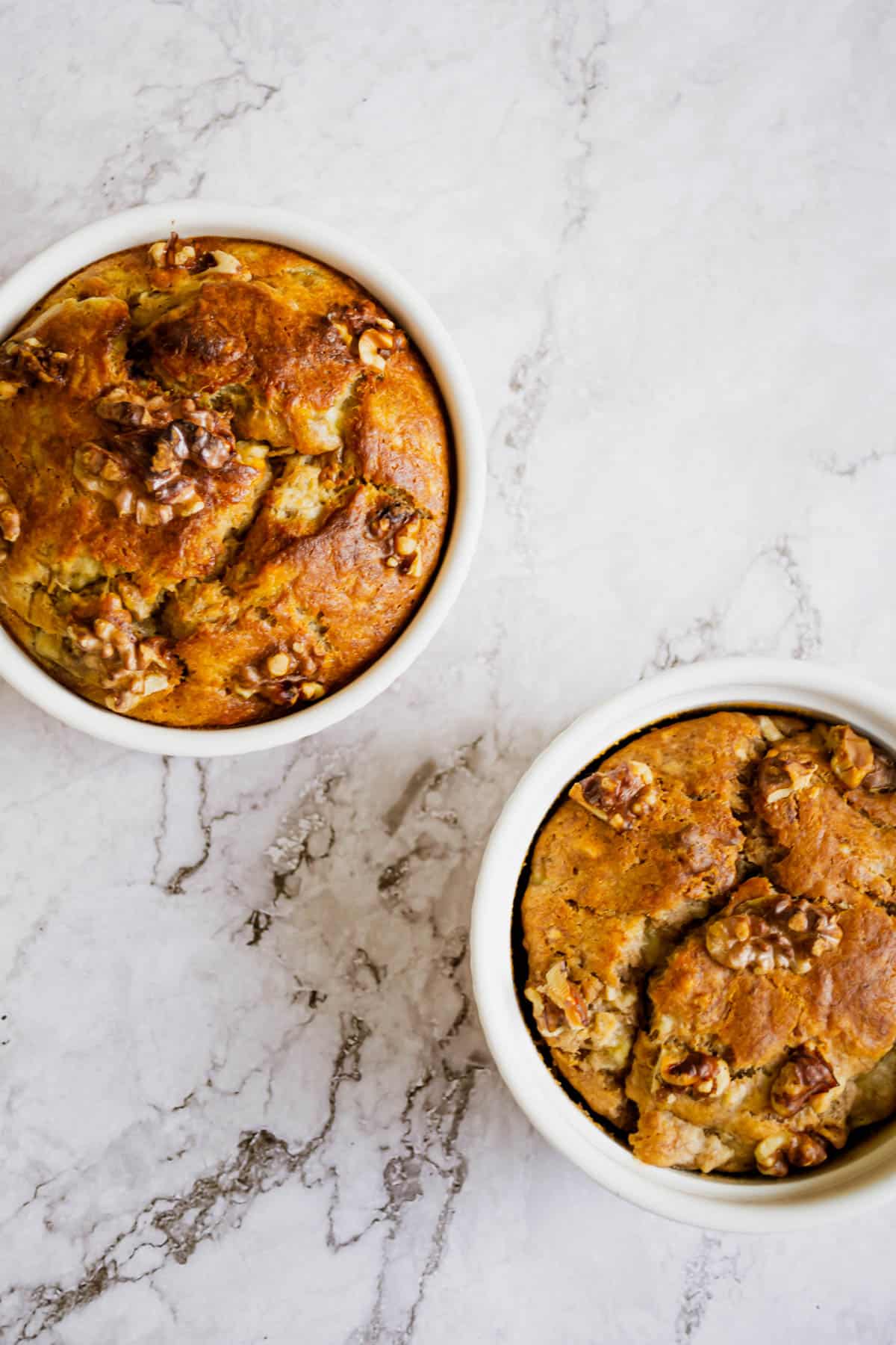 Overhead shot of two ramekins with banana bread in them on a marble table.