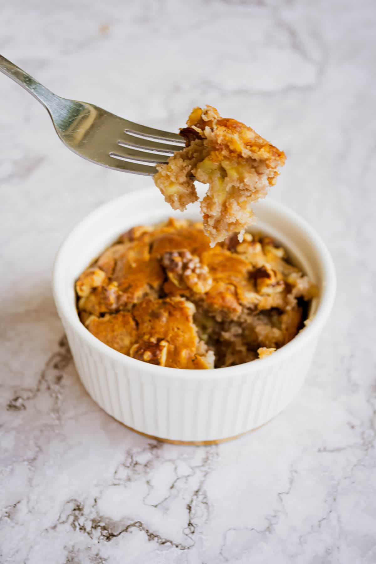 Fork taking a bite out of single serve banana bread with a ramekin of banana bread in the background.