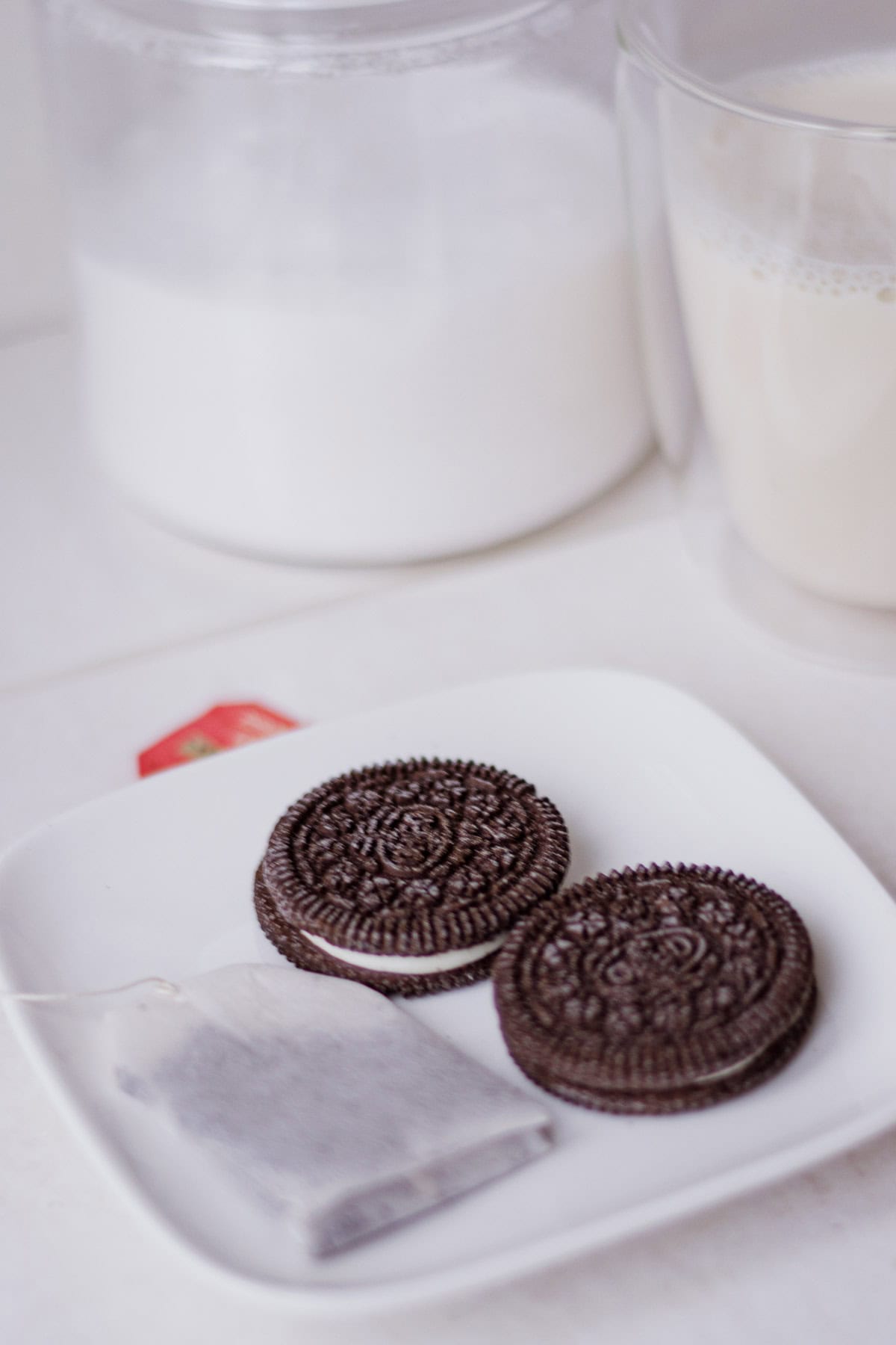 Overhead view of Oreos on a plate with a tea bag, with sugar and soy milk in the background.