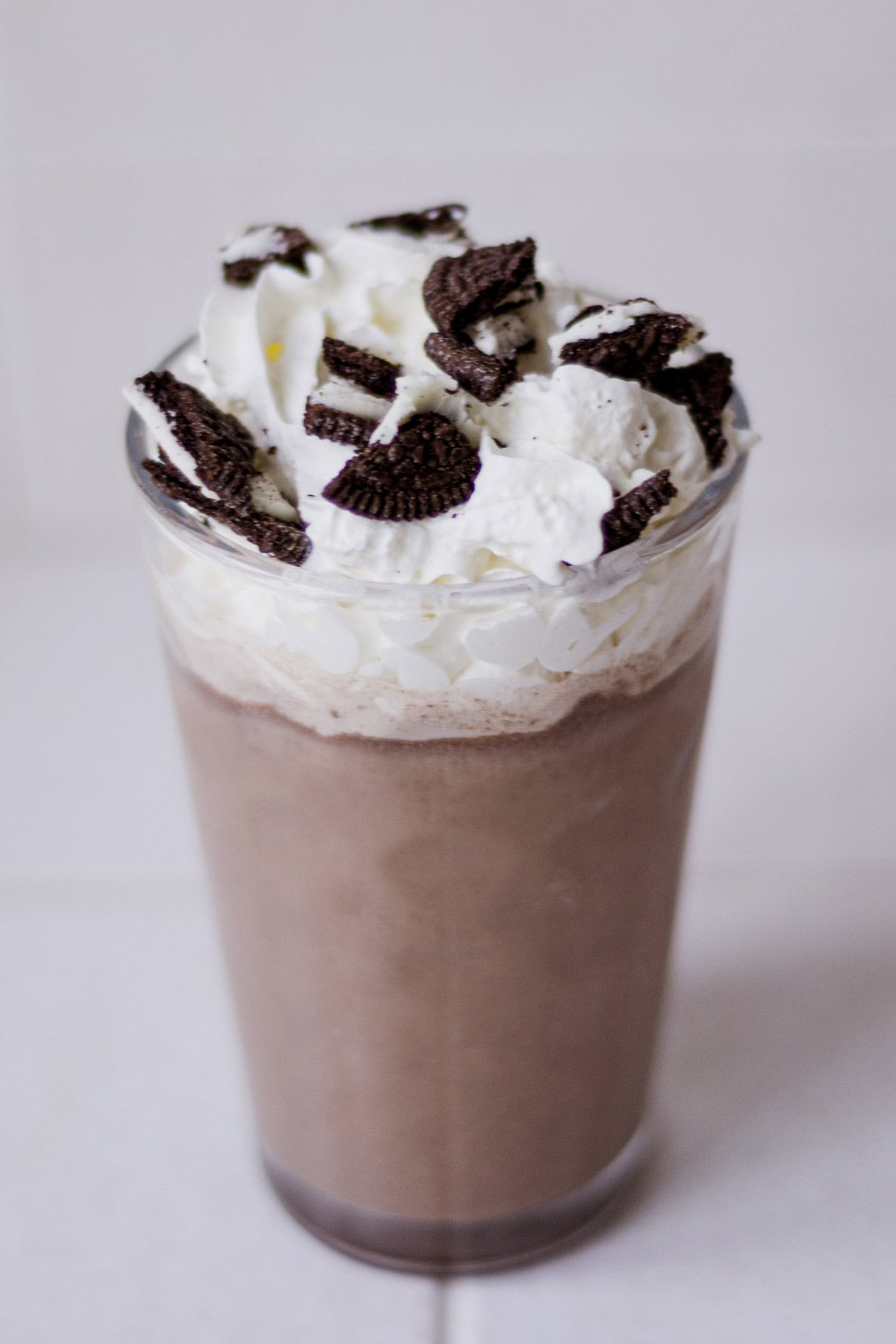 Oreo milk tea in a glass, topped with whipped cream and a crushed Oreo.