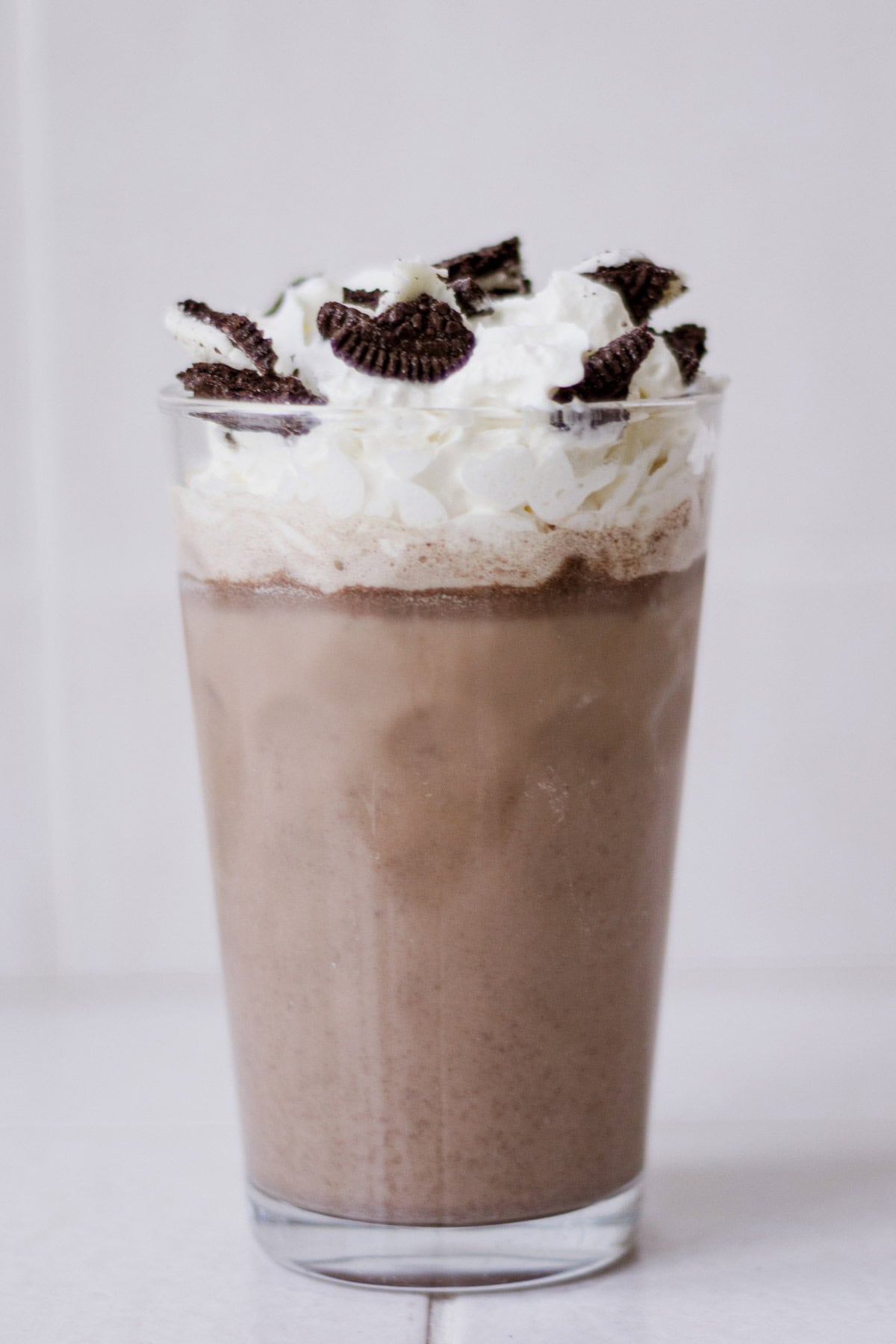 Front view of Oreo milk tea in a glass, topped with whipped cream and a crushed Oreo.