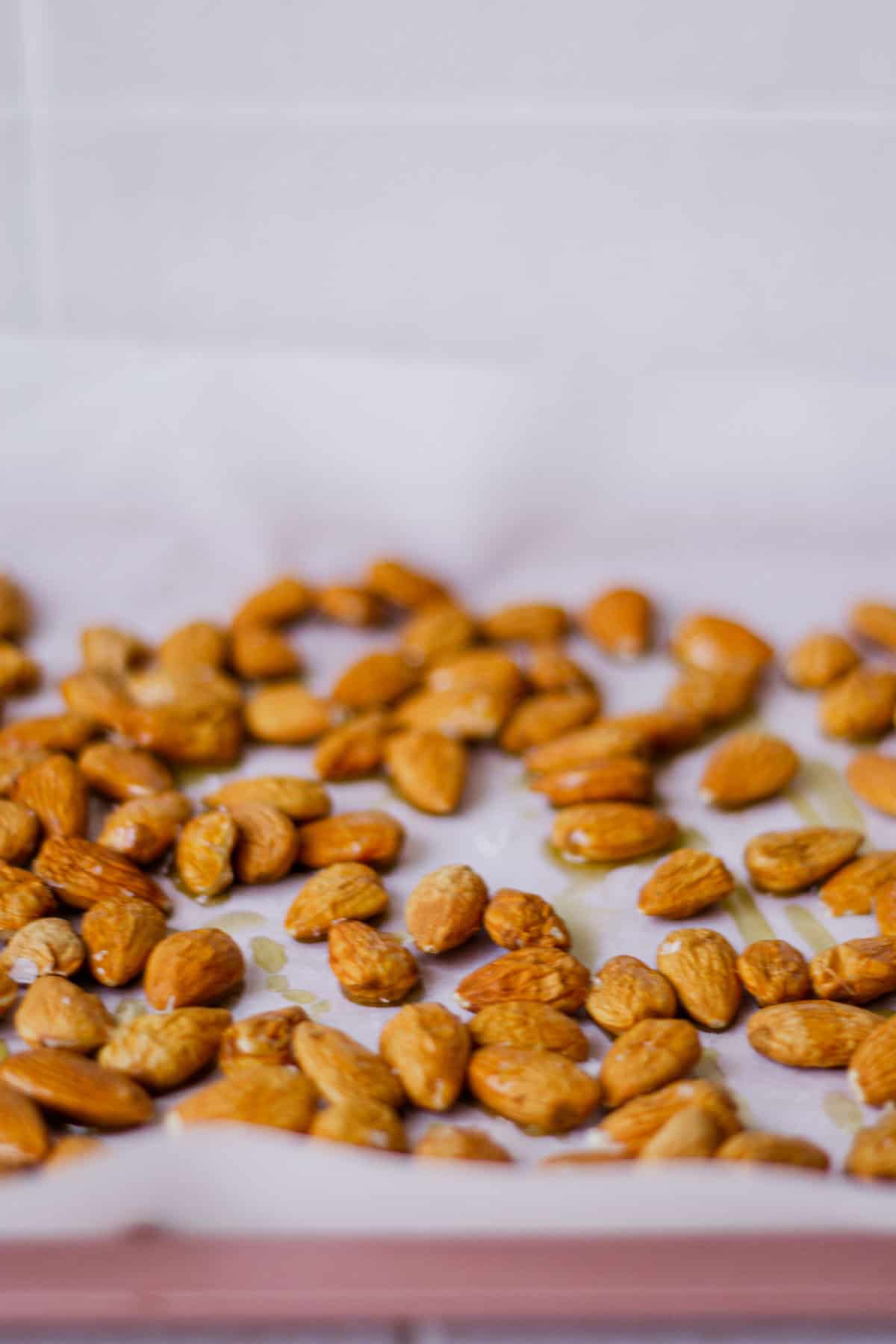 Side view of raw almonds, sprinkled with salt and olive oil on a baking tray lined with parchment paper.