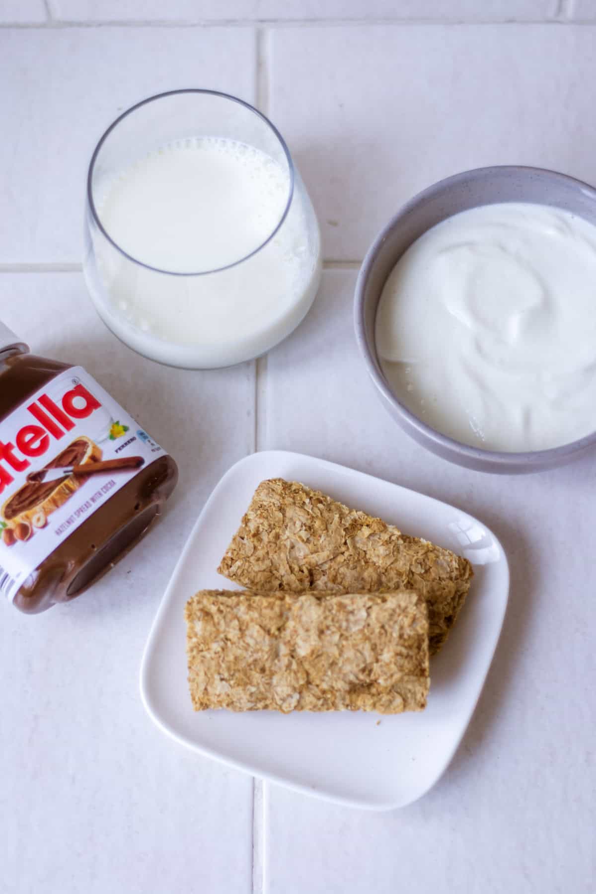 Overhead shot of ingredients to make Nutella overnight Weetabix, going clockwise from the top centre: milk, greek yoghurt, weetabix/weetbix, Nutella.