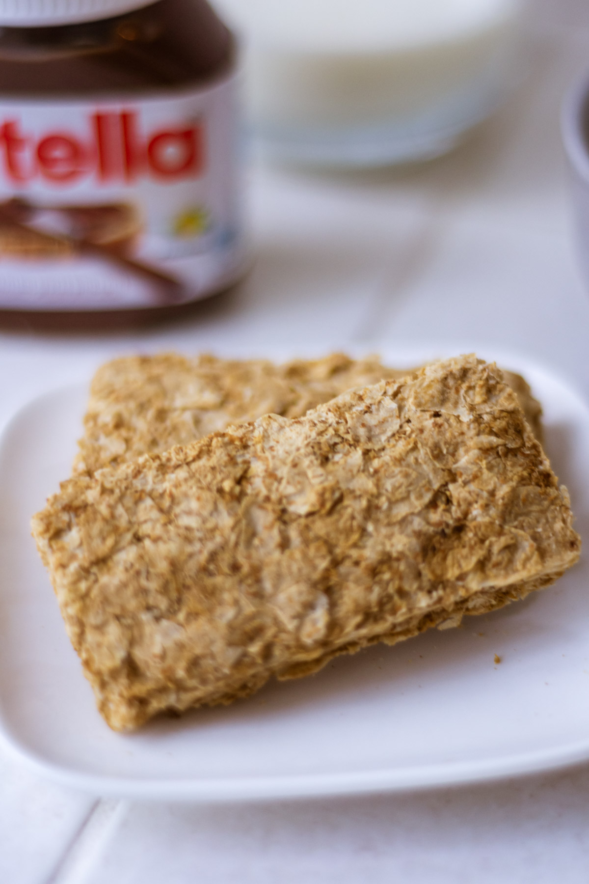Close up shot of Weetbix/Weetabix with a blurred image of a Nutella jar in the background.