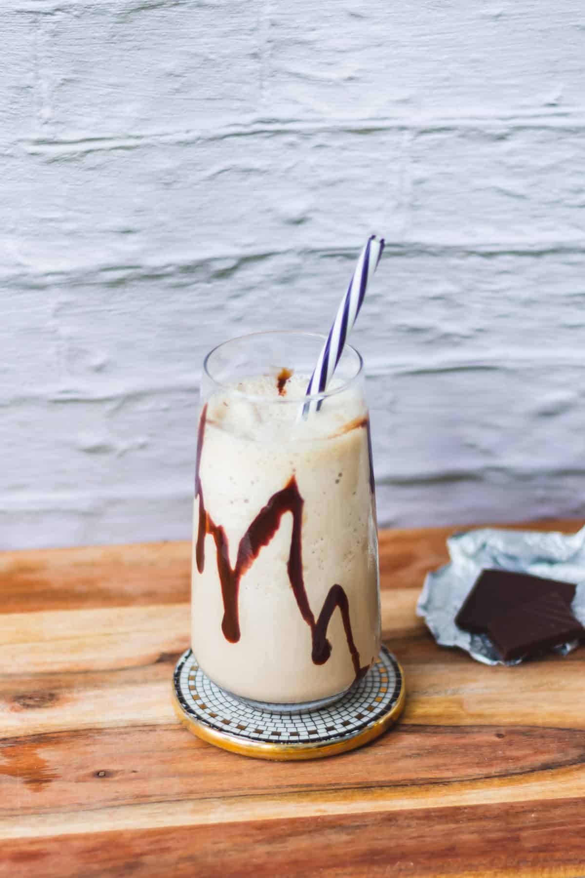 Mocha shake in a tall glass with chocolate squares in the background.