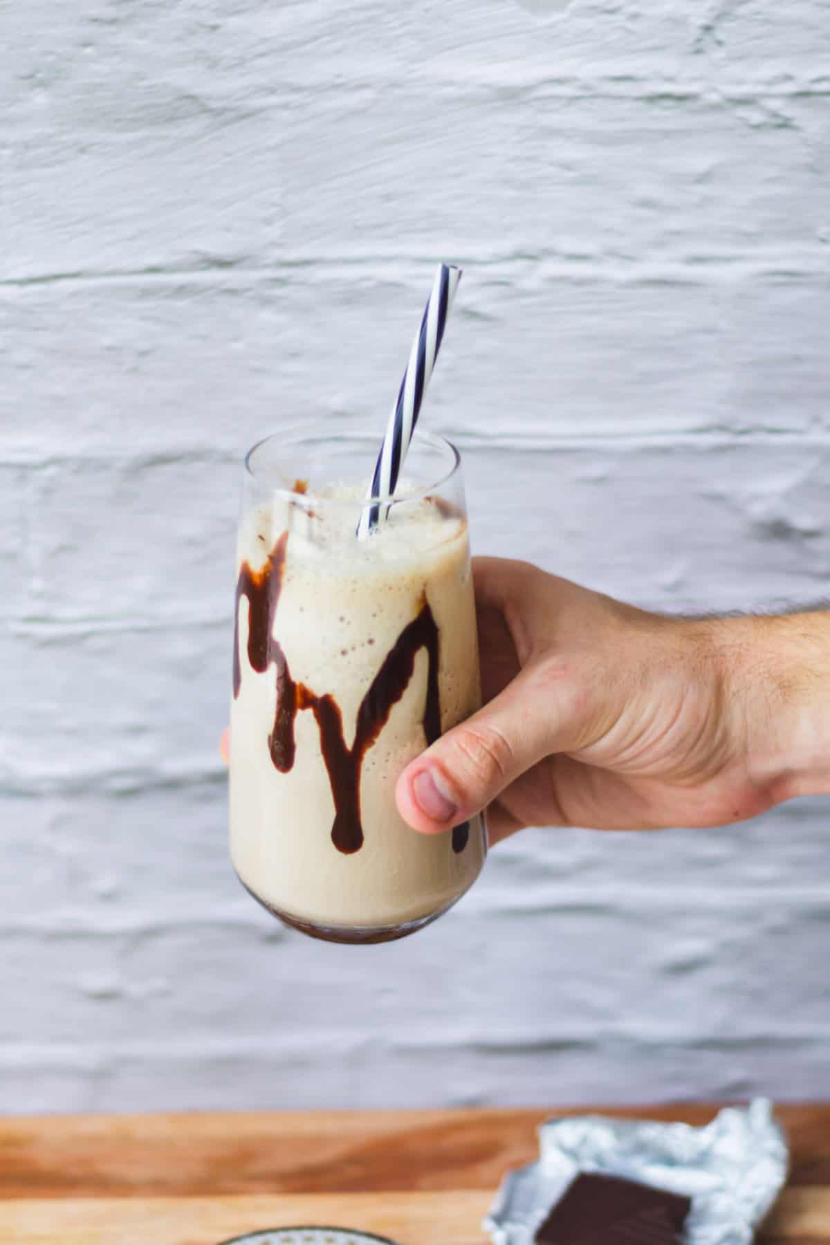 Hand holding a mocha shake in front of a white brick wall