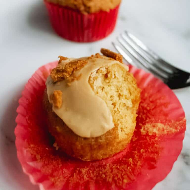 Vanilla cupcake with cream cheese frosting in pink cupcake liner on white marble surface with fork in background.