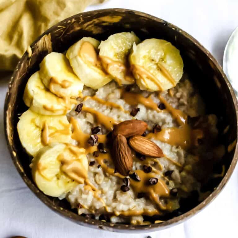 Creamy oatmeal topped with sliced bananas, almond butter, dark chocolate chips, and whole almonds, served in a rustic bowl - a healthy, delicious breakfast or snack.