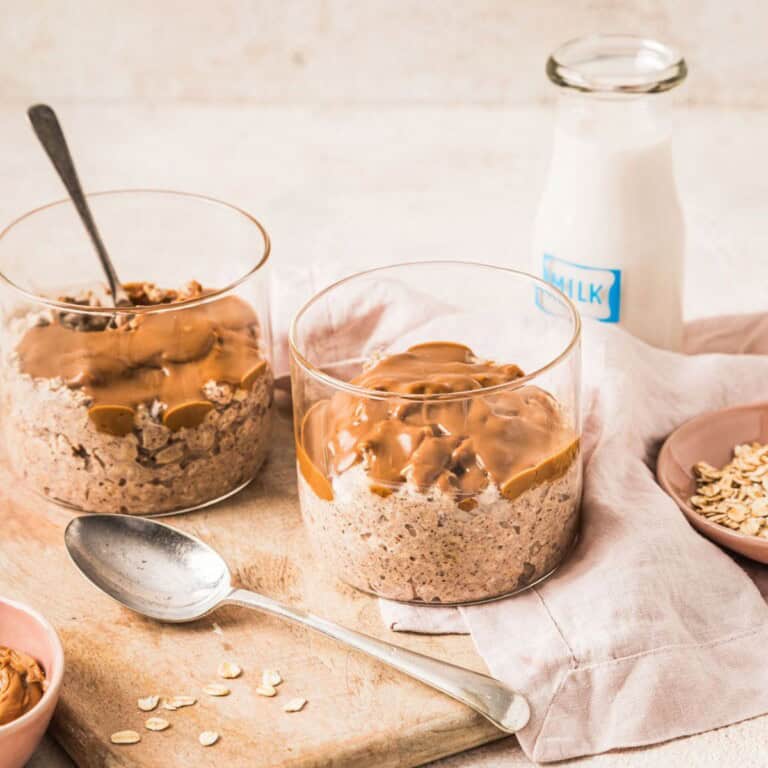 Creamy peanut butter oatmeal jars topped with chocolate and peanut butter, served with a glass of milk, on a rustic wooden table for a healthy breakfast.