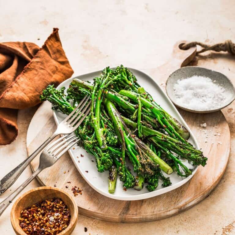 Grilled asparagus on a white plate with seasoning, served with crushed red pepper flakes and sea salt, arranged on a rustic wooden cutting board for healthy vegetarian meal options.