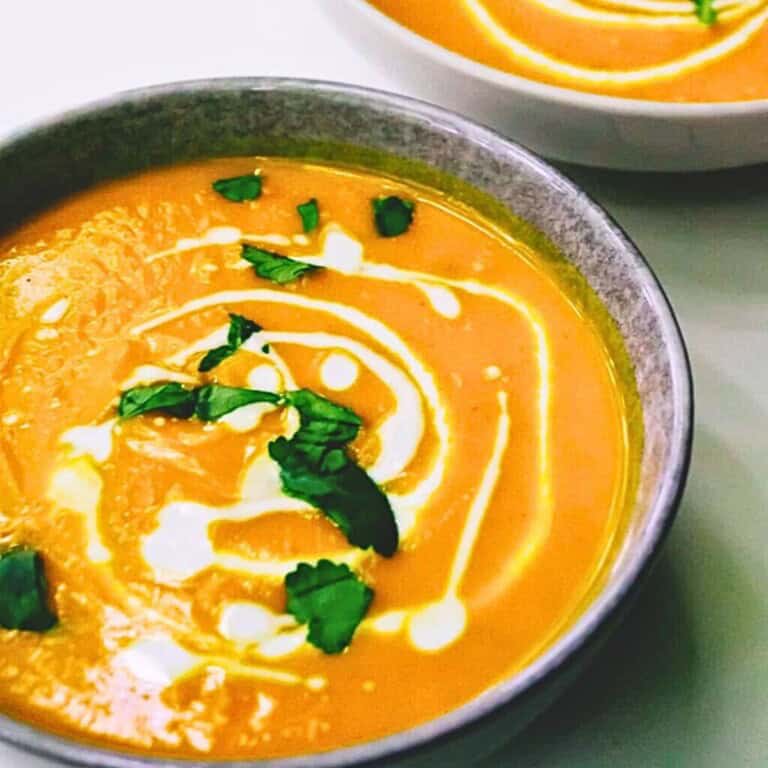 Creamy carrot ginger soup garnished with fresh cilantro and a swirl of cream, served in a rustic bowl. Perfect for healthy, homemade soups and comforting meals.