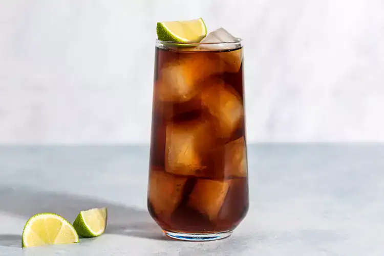 Rum and Coke served on ice in a highball glass with a slice of lime.