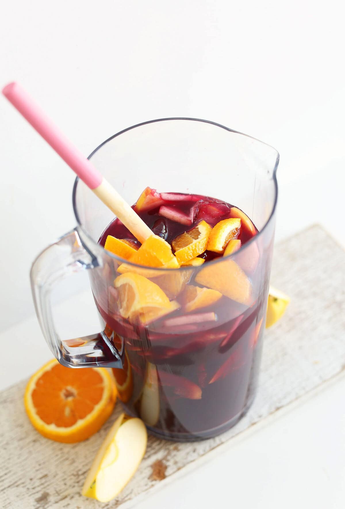 Pitcher of sangria, including dark red sangria, orange and apple slices.