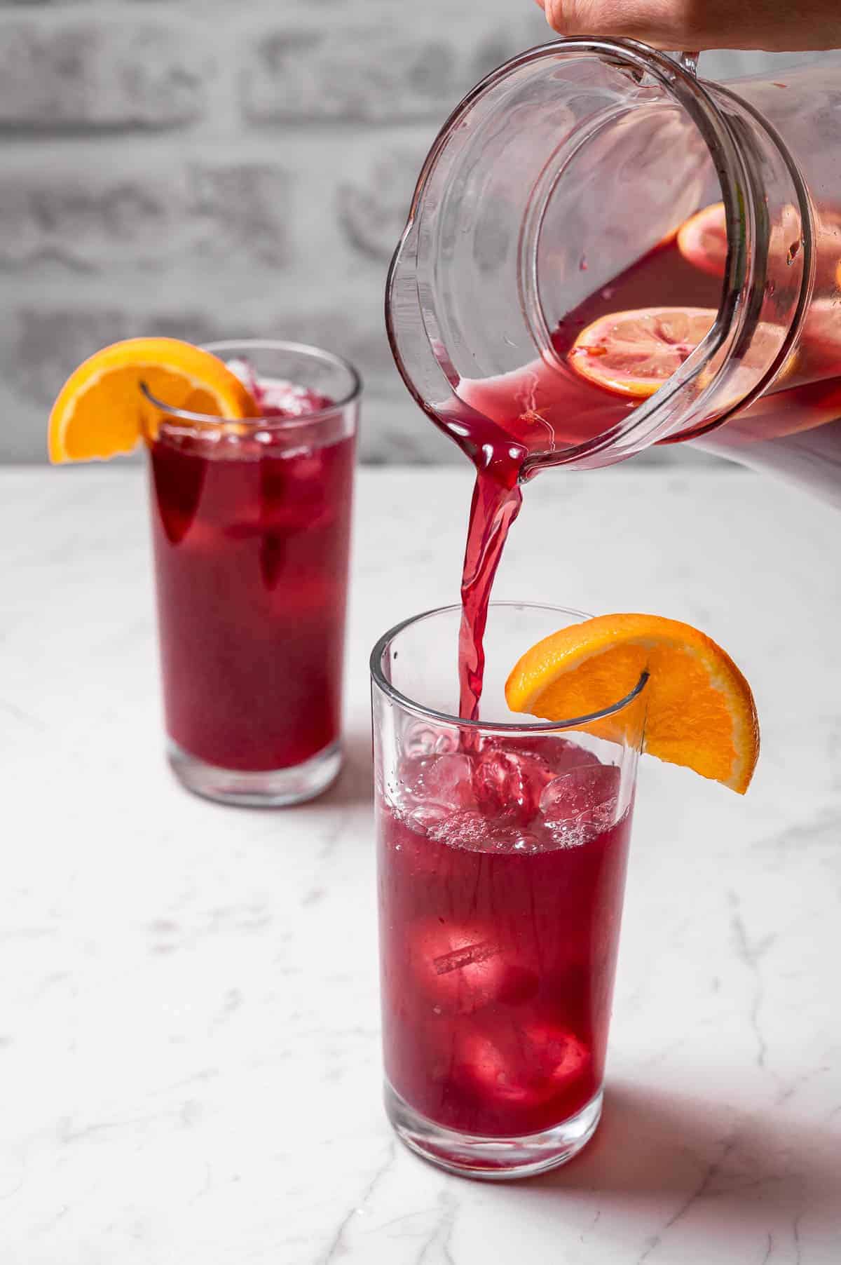 Tinto de Verano being poured into two tall glasses from a pitcher, served with orange wedges.